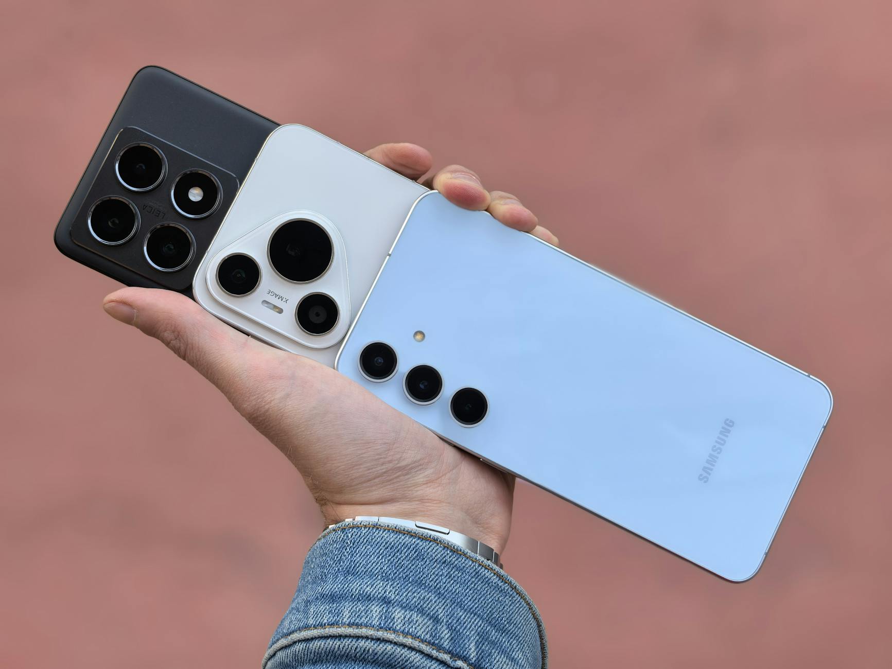 Dłoń trzyma trzy smartfony z różnymi wyspami aparatów