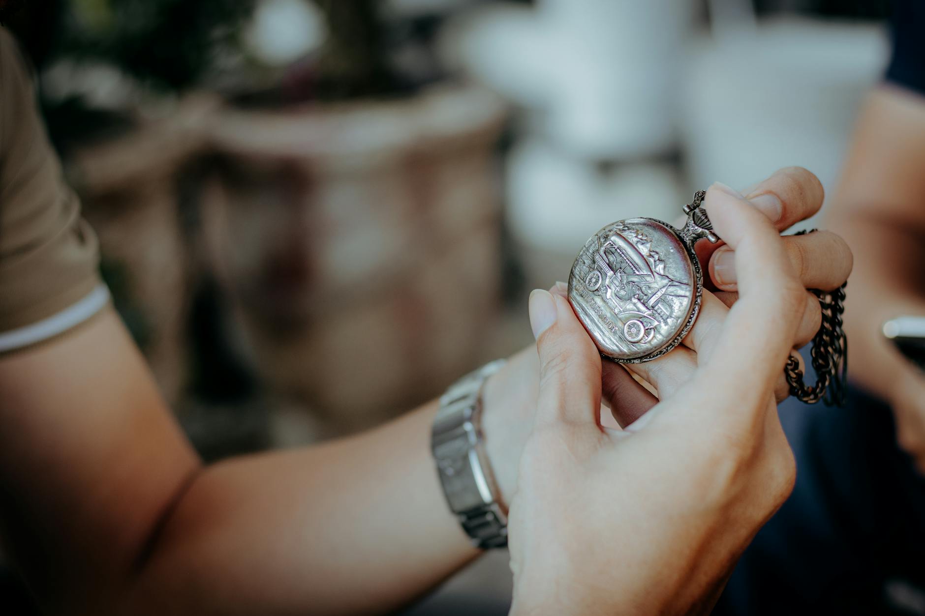 Dłonie trzymające zabytkowy zegarek kieszonkowy na łańcuszku na dworze