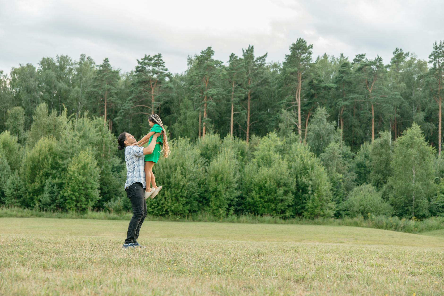 Ojciec podrzuca córkę w zielonym lesie podczas wspólnej zabawy