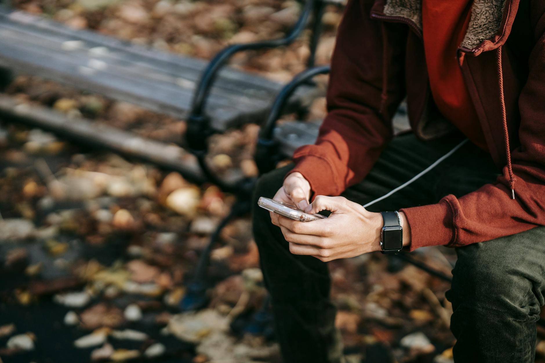 Mężczyzna w jesiennym parku pisze na smartfonie, obok na nadgarstku smartwatch