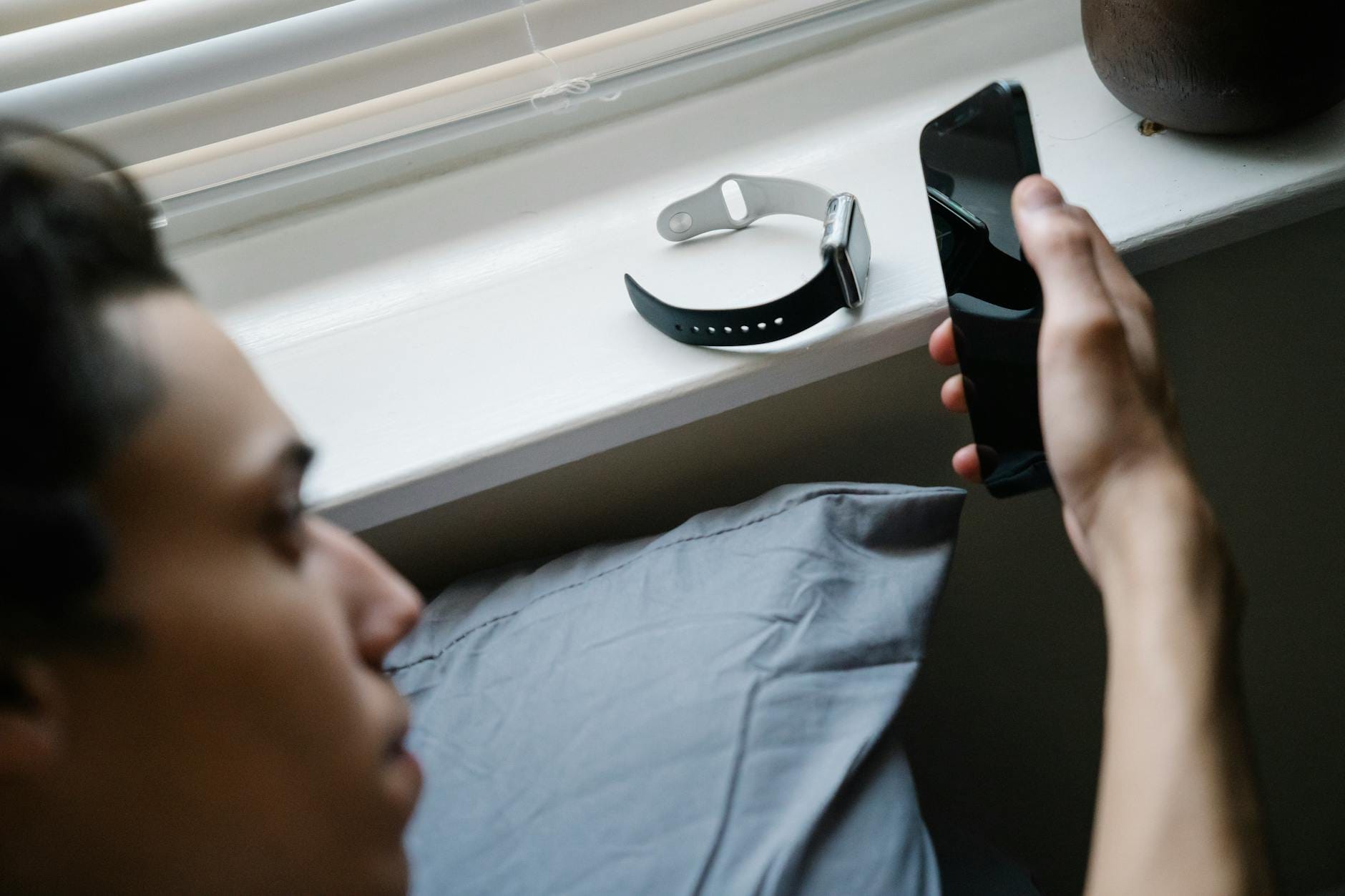 Smartwatch leżący na parapecie obok osoby korzystającej ze smartfona