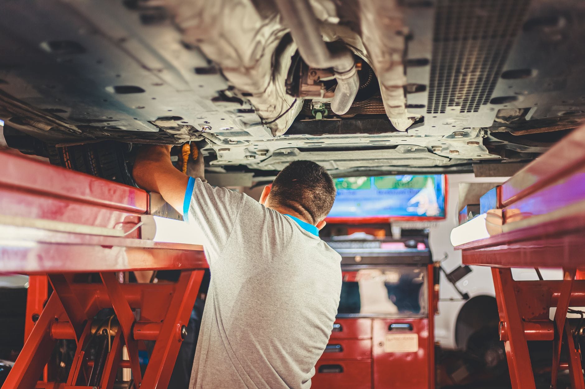 Mechanik naprawia podniesione auto na podnośniku w warsztacie