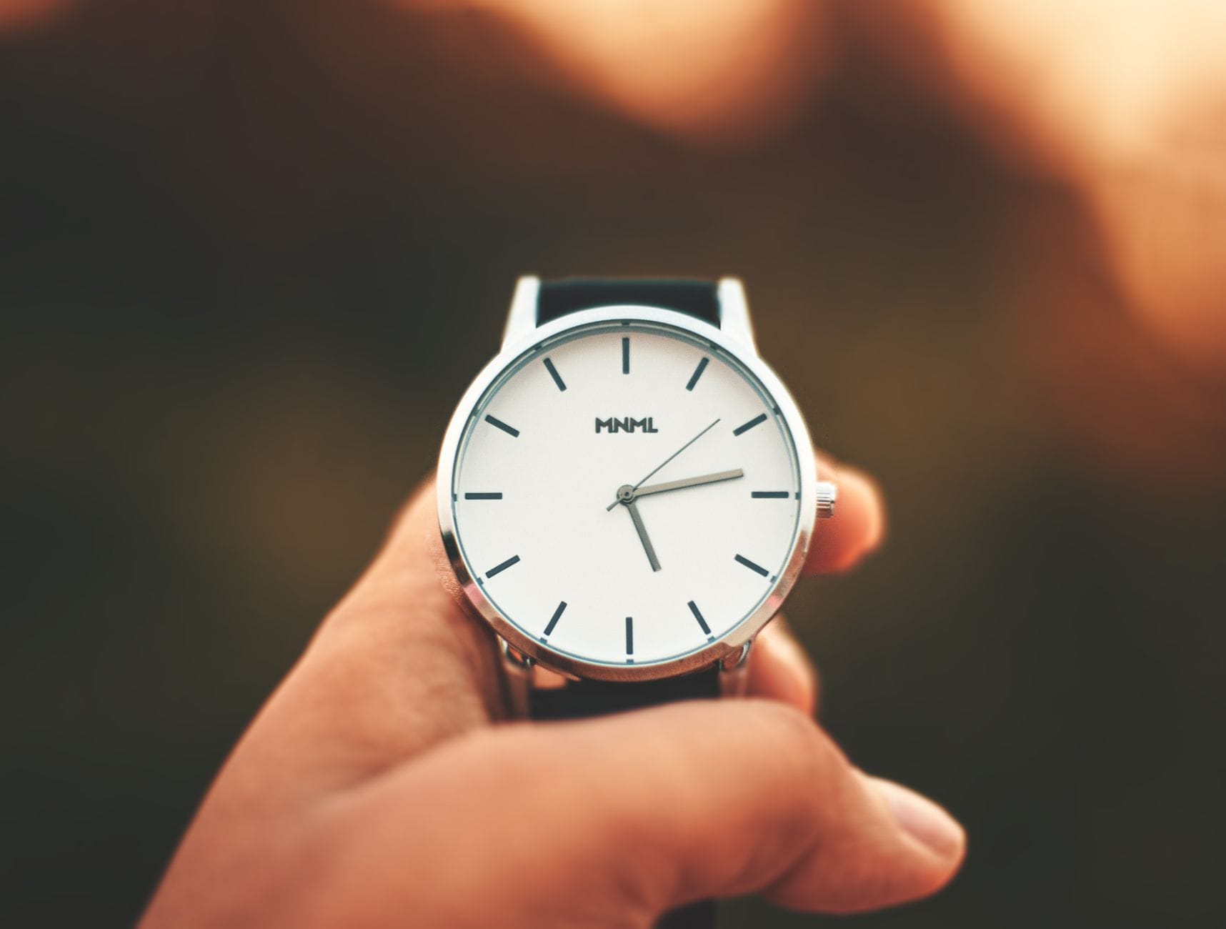 Minimalistyczny zegarek analogowy trzymany w dłoni z rozmytym tłem